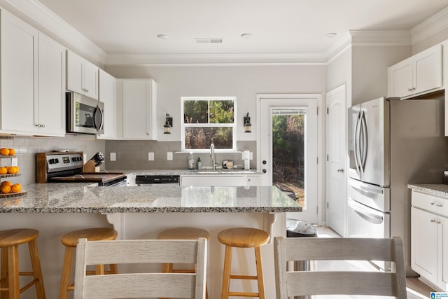 kitchen featuring white cabinets, a kitchen breakfast bar, stainless steel appliances, and light stone countertops