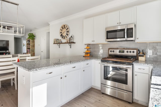 kitchen with kitchen peninsula, ornamental molding, appliances with stainless steel finishes, tasteful backsplash, and white cabinetry