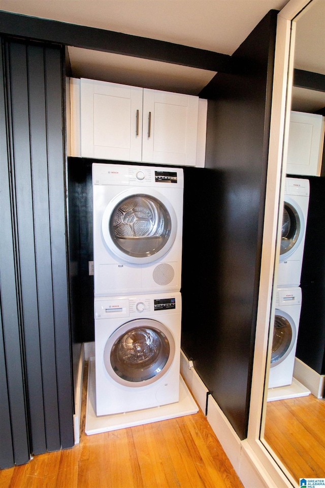 laundry room with light hardwood / wood-style floors, cabinets, and stacked washing maching and dryer