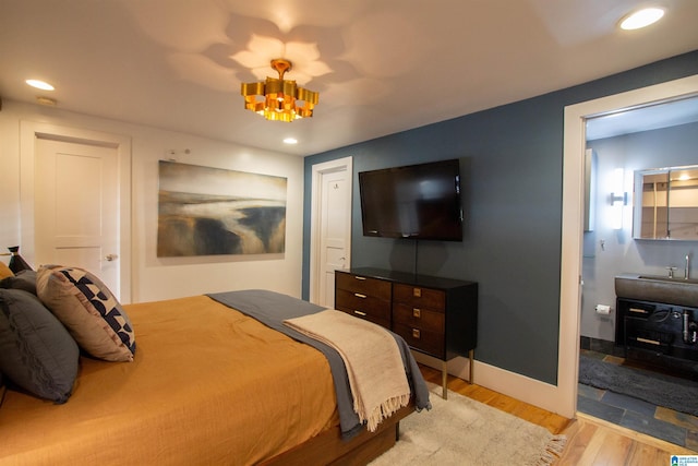 bedroom featuring a chandelier, connected bathroom, and light hardwood / wood-style flooring