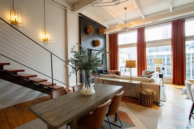 dining space featuring a notable chandelier, beam ceiling, a high ceiling, and light hardwood / wood-style flooring