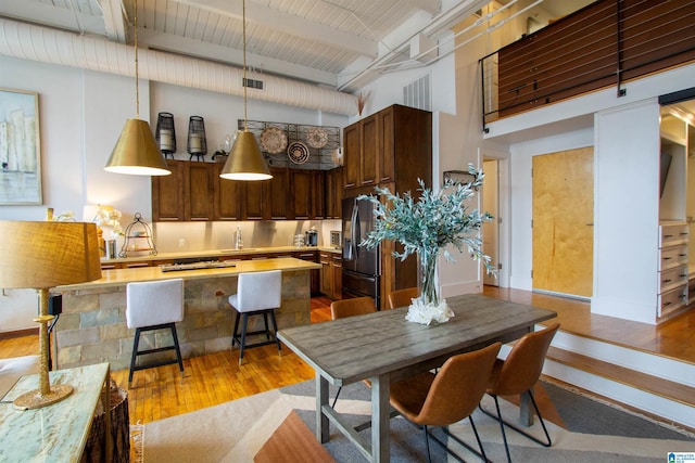 kitchen with a high ceiling, black fridge, beamed ceiling, pendant lighting, and light wood-type flooring