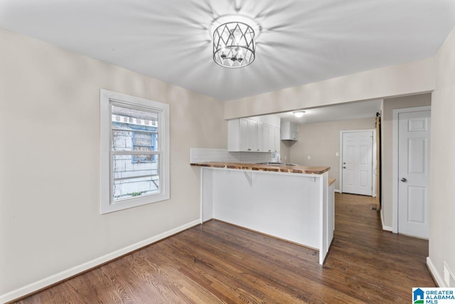 kitchen with dark wood-type flooring, kitchen peninsula, decorative backsplash, a barn door, and white cabinetry