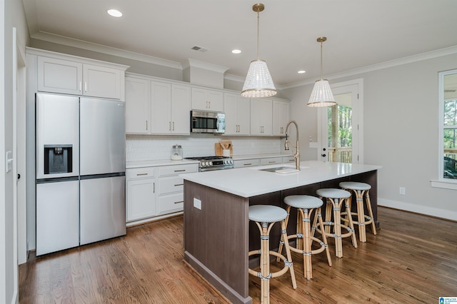 kitchen featuring stainless steel appliances, sink, decorative light fixtures, a center island with sink, and white cabinets