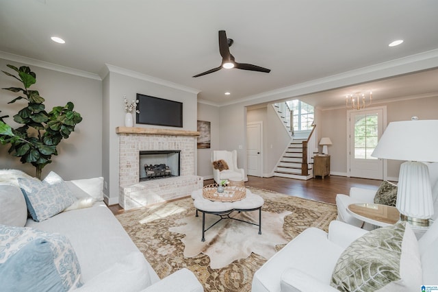 living room with a fireplace, hardwood / wood-style floors, ceiling fan with notable chandelier, and ornamental molding