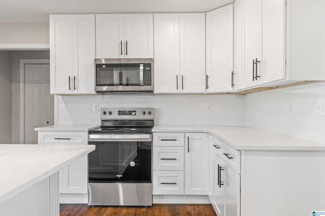 kitchen with light stone countertops, backsplash, stainless steel appliances, dark hardwood / wood-style floors, and white cabinetry