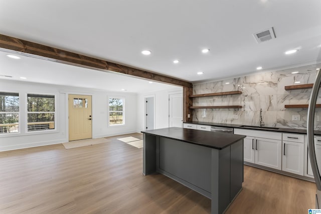 kitchen with sink, backsplash, hardwood / wood-style floors, a kitchen island, and beamed ceiling