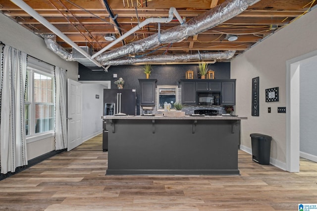 kitchen featuring hardwood / wood-style floors, an island with sink, gray cabinets, a breakfast bar, and black appliances