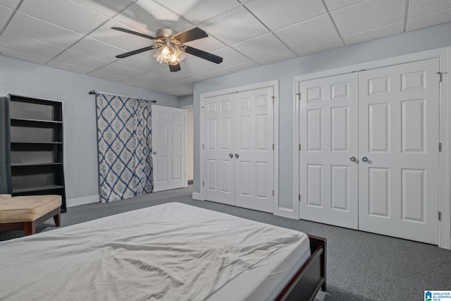 carpeted bedroom with multiple closets, ceiling fan, and a drop ceiling