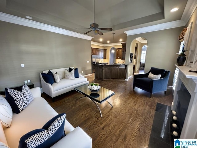 living room featuring dark hardwood / wood-style flooring, a raised ceiling, ceiling fan, and ornamental molding