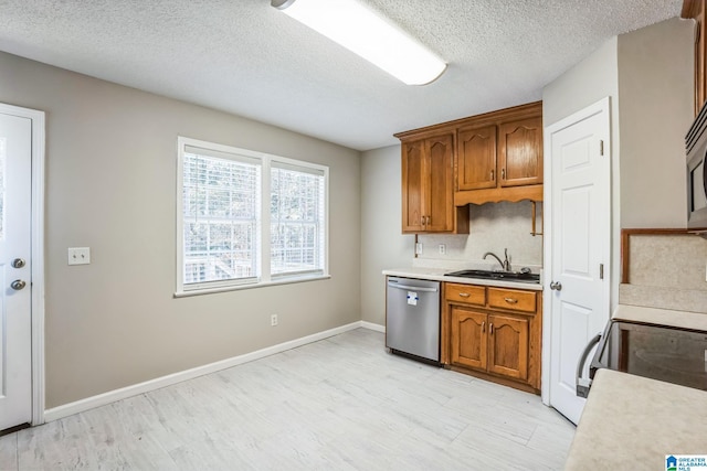 kitchen featuring light wood-type flooring, backsplash, stainless steel dishwasher, a textured ceiling, and sink