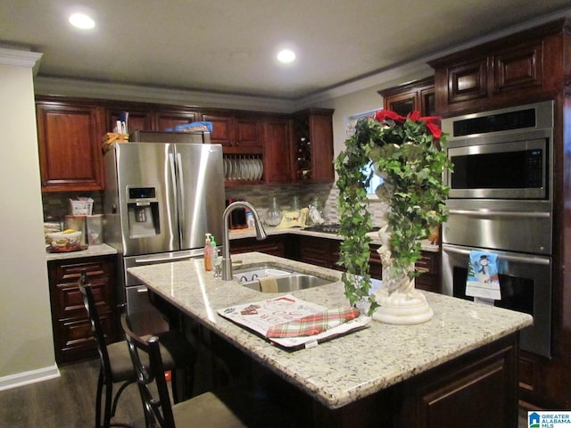 kitchen with a kitchen island with sink, dark wood-type flooring, sink, decorative backsplash, and appliances with stainless steel finishes