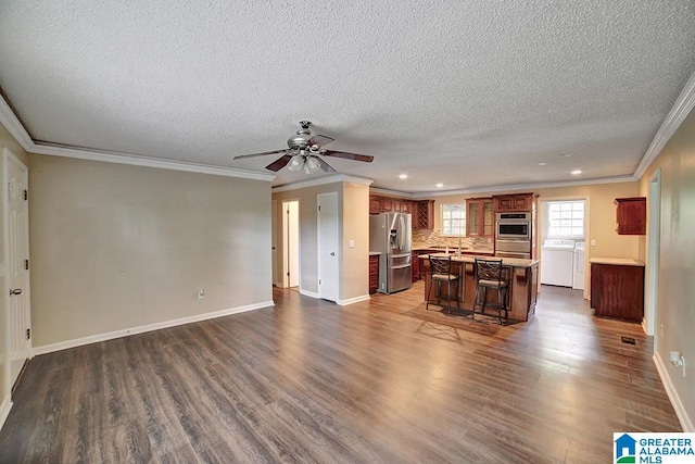 kitchen featuring a kitchen breakfast bar, ornamental molding, stainless steel appliances, washing machine and clothes dryer, and a center island