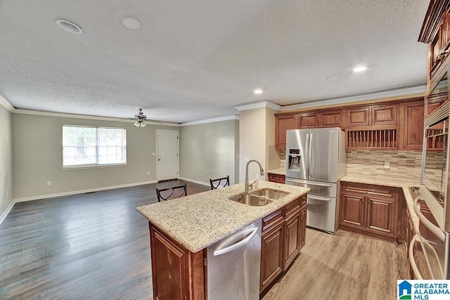 kitchen featuring sink, ceiling fan, an island with sink, appliances with stainless steel finishes, and light stone counters