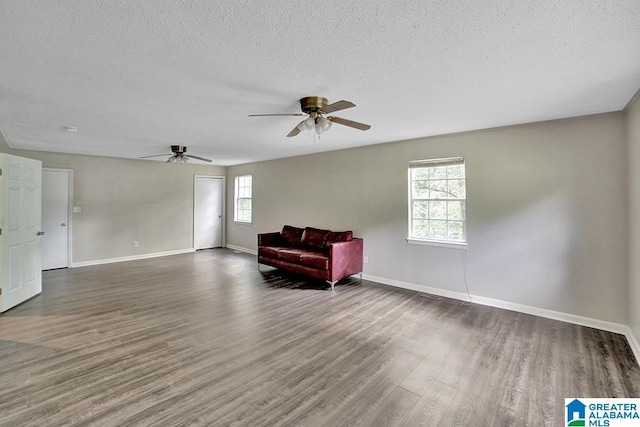 living area with a textured ceiling, a wealth of natural light, dark wood-type flooring, and ceiling fan