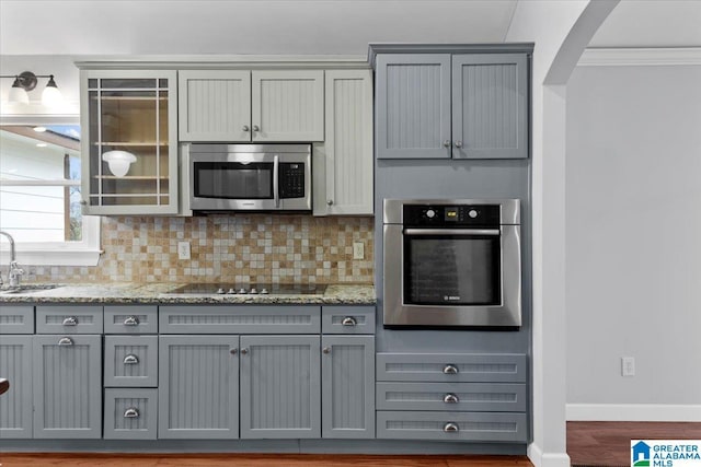 kitchen featuring stainless steel appliances, gray cabinetry, backsplash, and light stone counters