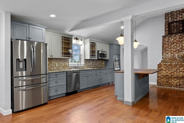 kitchen with stainless steel appliances, light stone counters, pendant lighting, brick wall, and backsplash