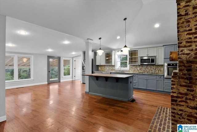 kitchen with a center island, gray cabinets, pendant lighting, stainless steel appliances, and decorative backsplash