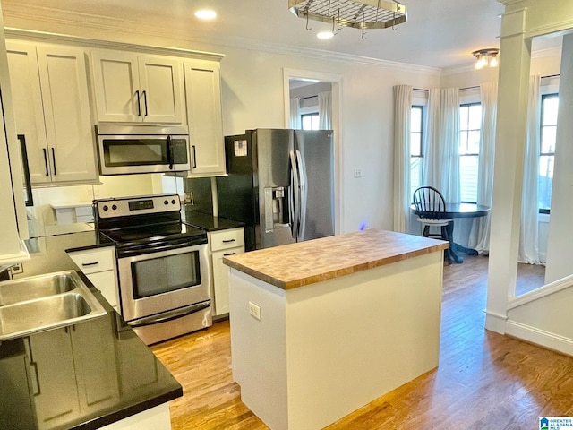 kitchen featuring sink, appliances with stainless steel finishes, crown molding, a kitchen island, and light wood-type flooring