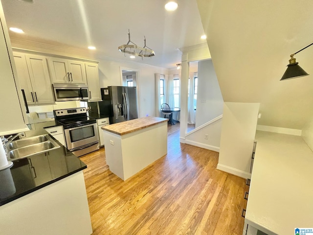 kitchen with wooden counters, stainless steel appliances, a kitchen island, sink, and white cabinetry