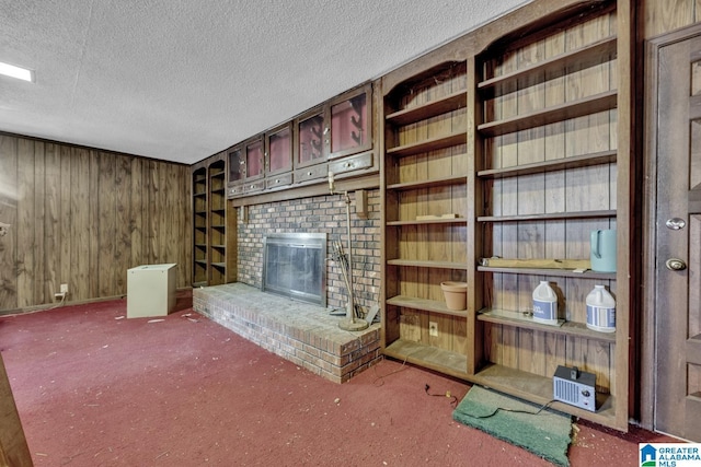 unfurnished living room with carpet flooring, wood walls, a textured ceiling, and a brick fireplace