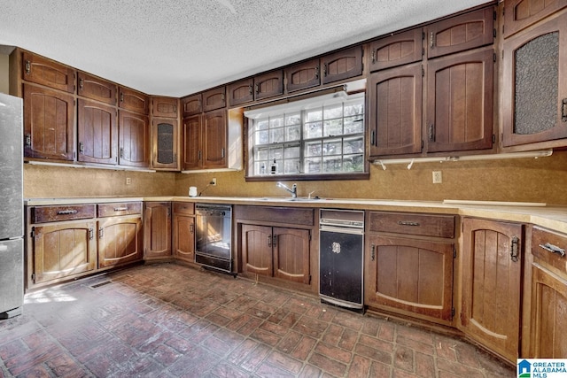 kitchen featuring a textured ceiling, stainless steel fridge, sink, and black dishwasher