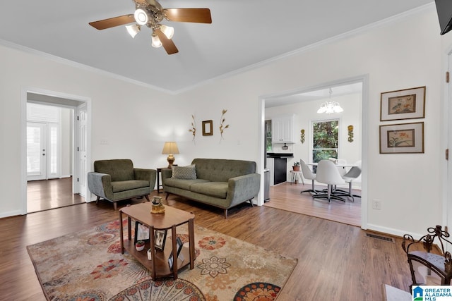 living room with ceiling fan with notable chandelier, wood-type flooring, and ornamental molding