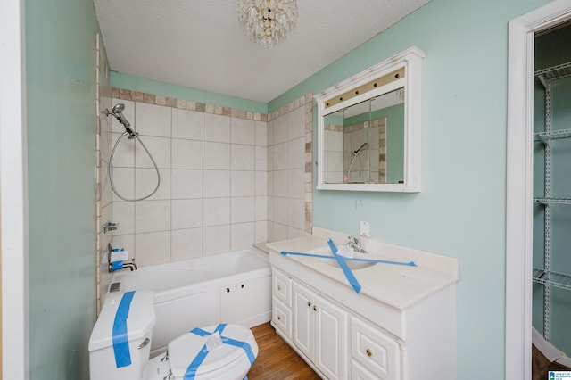 full bathroom with wood-type flooring, a textured ceiling, toilet, vanity, and tiled shower / bath