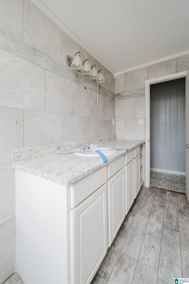 bathroom featuring vanity, crown molding, a textured ceiling, and tile walls