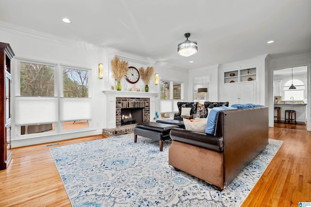 living room featuring a fireplace, built in features, crown molding, and sink