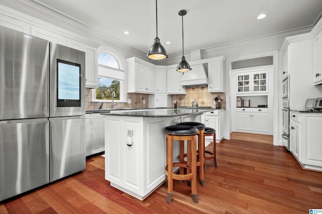 kitchen featuring custom exhaust hood, white cabinets, appliances with stainless steel finishes, decorative light fixtures, and a kitchen island