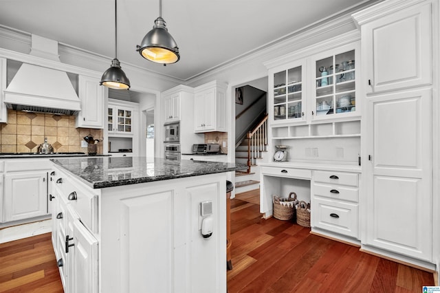 kitchen with glass insert cabinets, custom range hood, decorative light fixtures, and white cabinetry