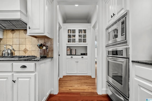 kitchen with a warming drawer, appliances with stainless steel finishes, glass insert cabinets, white cabinets, and dark stone countertops