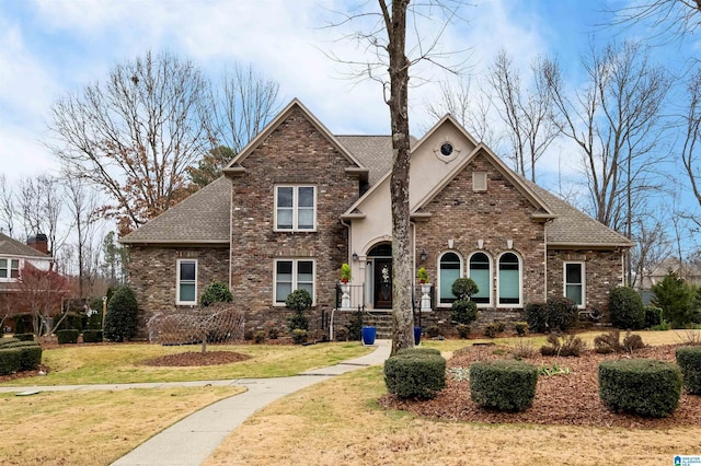 traditional home featuring a shingled roof, a front yard, brick siding, and stucco siding