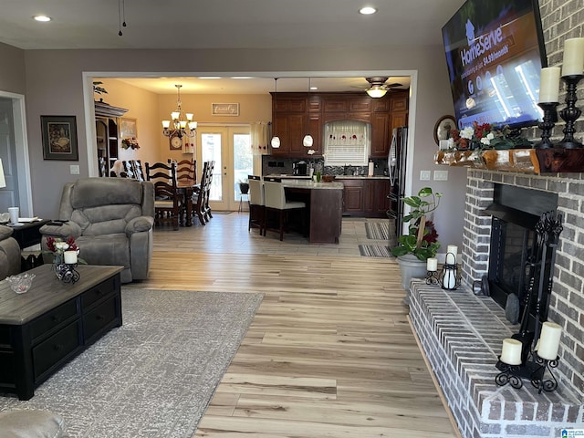 living room with ceiling fan with notable chandelier, light wood-type flooring, sink, and a brick fireplace