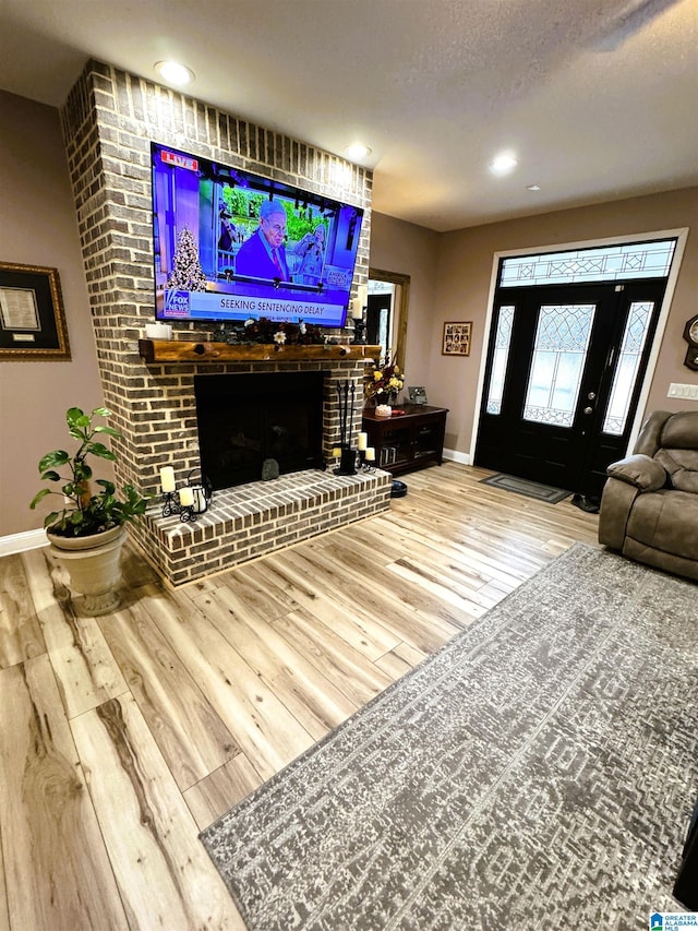 living room featuring wood-type flooring, a textured ceiling, and a brick fireplace