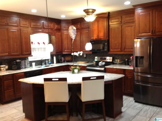 kitchen featuring light stone counters, a breakfast bar, black appliances, a kitchen island, and hanging light fixtures