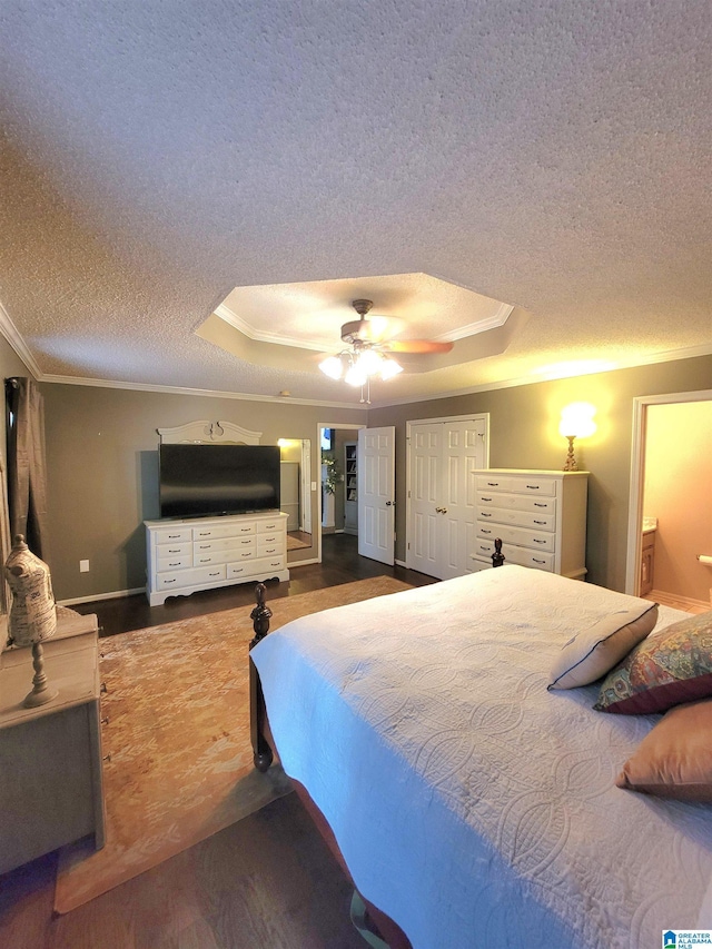 bedroom featuring connected bathroom, ceiling fan, dark wood-type flooring, crown molding, and a tray ceiling