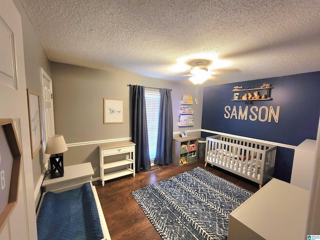 bedroom with ceiling fan, dark hardwood / wood-style flooring, a textured ceiling, and a nursery area