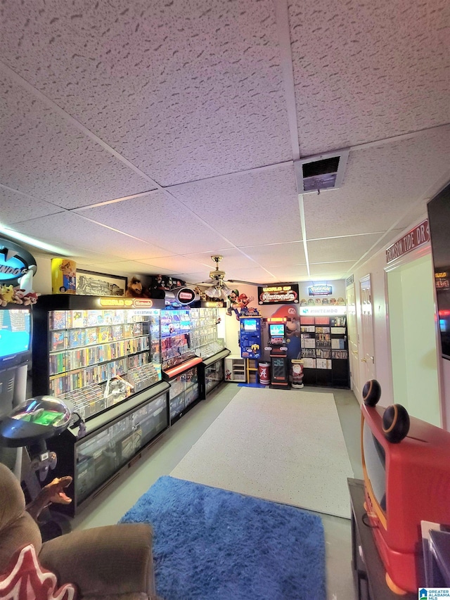 recreation room with concrete flooring, a paneled ceiling, and ceiling fan