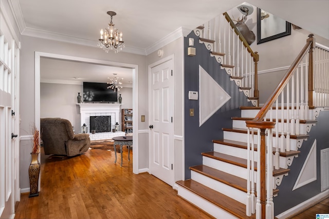 stairway featuring hardwood / wood-style flooring, a notable chandelier, ornamental molding, and a brick fireplace