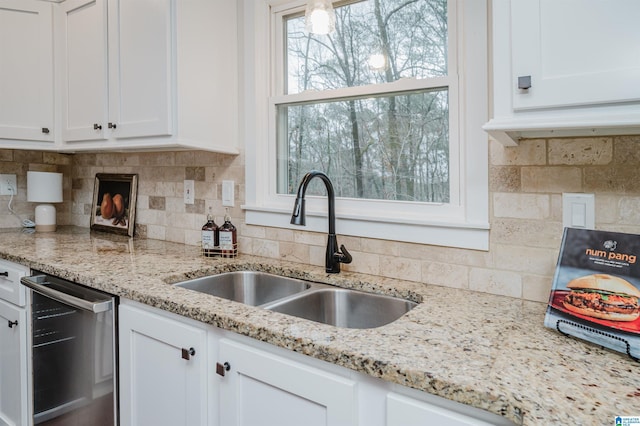 kitchen featuring white cabinetry, dishwasher, light stone countertops, sink, and decorative backsplash