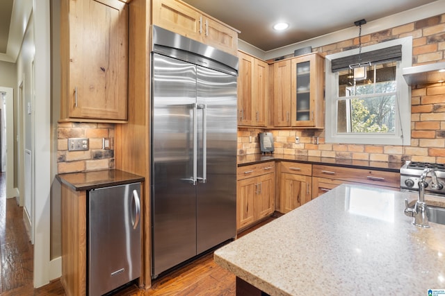 kitchen with light stone countertops, tasteful backsplash, pendant lighting, built in refrigerator, and stainless steel refrigerator