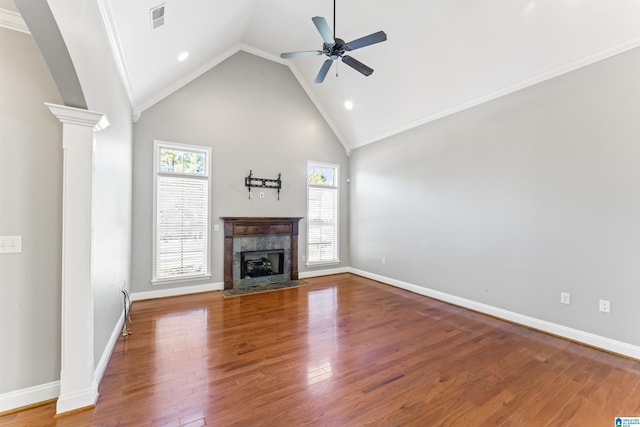 unfurnished living room featuring a tile fireplace, hardwood / wood-style flooring, ceiling fan, ornamental molding, and ornate columns