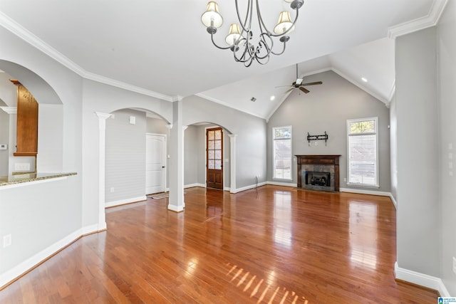 unfurnished living room featuring decorative columns, ceiling fan with notable chandelier, vaulted ceiling, crown molding, and wood-type flooring