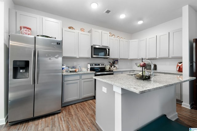 kitchen featuring appliances with stainless steel finishes, light stone counters, sink, light hardwood / wood-style flooring, and an island with sink