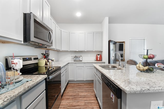 kitchen with a kitchen island with sink, light stone countertops, sink, and appliances with stainless steel finishes