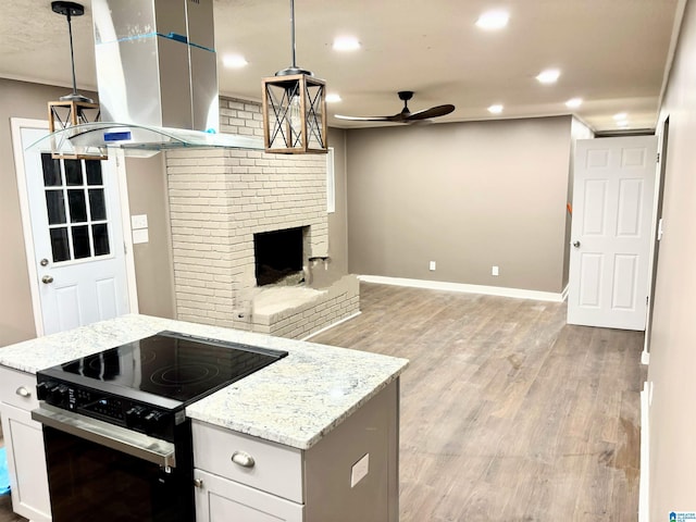 kitchen with pendant lighting, ceiling fan, a fireplace, electric range oven, and island exhaust hood