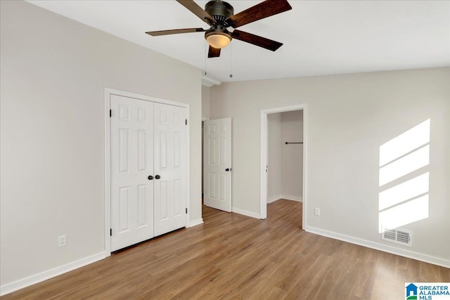 unfurnished bedroom with ceiling fan, vaulted ceiling, a closet, and light wood-type flooring