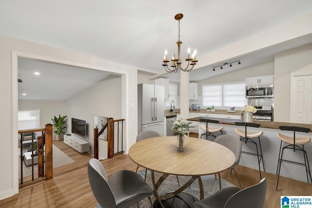 dining area featuring light wood-type flooring, vaulted ceiling, a wealth of natural light, and an inviting chandelier